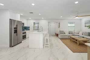 A modern kitchen with white cabinetry, a stainless steel refrigerator, and a central island. - The Beach Bungalow - Heated Pool (Fort Myers Beach)