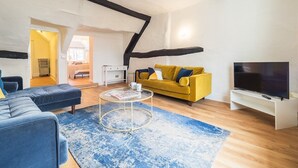 A modern living room with a yellow sofa, a blue sectional, a round coffee table, and a TV on a white stand.