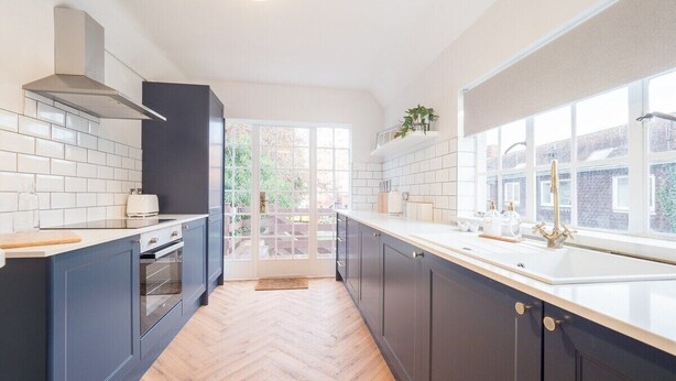 A modern kitchen with dark cabinets, a herringbone floor, and a large window providing natural light.