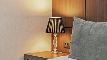 Habitación de hotel con cama, mesita de noche, lámpara y cabecera de madera.