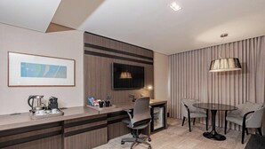 Een moderne hotelkamer met een bureau, stoelen, een televisietoestel en een schilderij aan de muur.