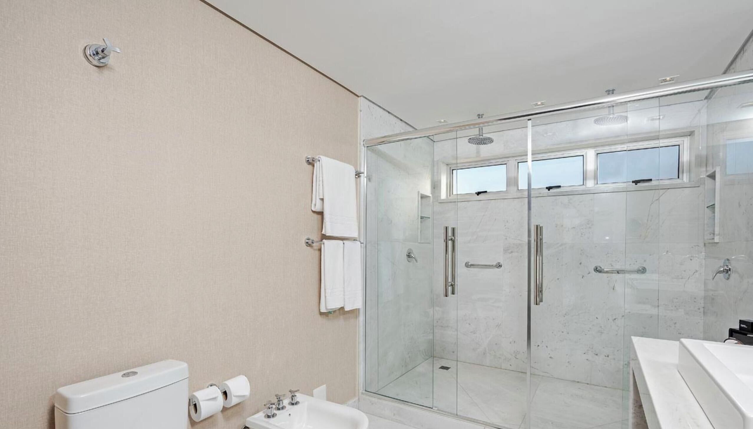 Et moderne badeværelse med en glasbrusekabine, en hvid vask og et toilet.