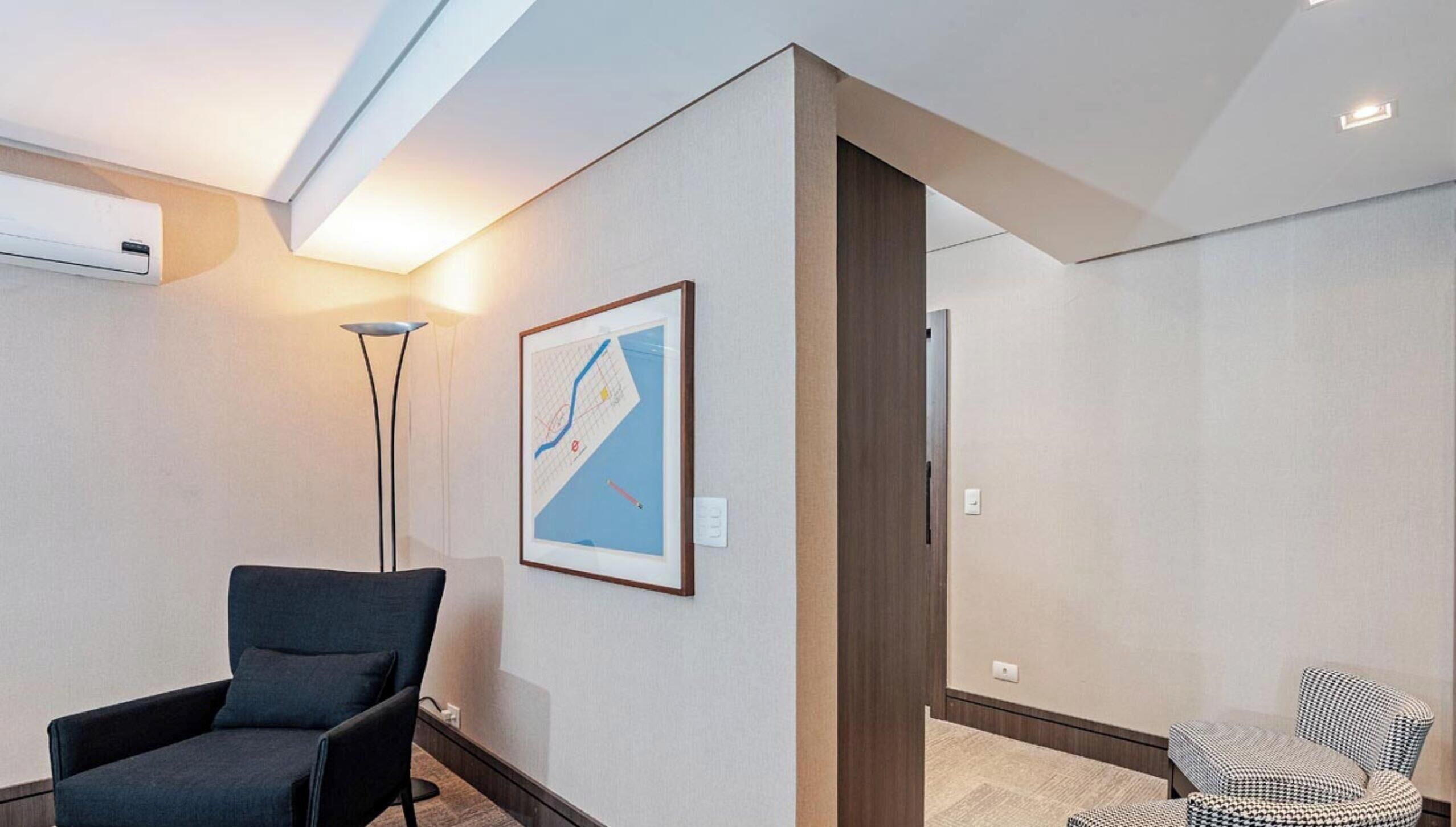 Una habitación de hotel moderna con un sillón de color oscuro, una lámpara de pie y un mapa enmarcado en la pared.