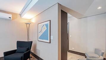 Una habitación de hotel moderna con un sillón de color oscuro, una lámpara de pie y un mapa enmarcado en la pared.