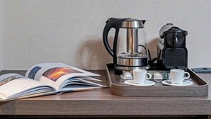 A neatly arranged hotel room with a framed abstract painting on the wall, a coffee maker, a kettle, and a tray with cups and saucers.
