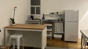 Une cuisine compacte avec un îlot central en bois, des tabourets blancs, un réfrigérateur et une fenêtre.