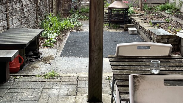 Un espace extérieur aménagé en terrasse, avec un sol en briques, des tables et des chaises en bois.
