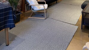 Un salon avec un canapé noir, un fauteuil blanc, une table basse, un mur en briques et une fenêtre.