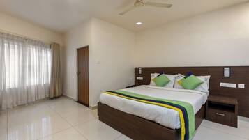 A hotel room with a bed, a nightstand, a ceiling fan, and a window with curtains.