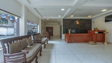 A reception area with a reception desk, a wall-mounted TV, and a reception counter. There are wooden chairs and a sofa arranged for guests.