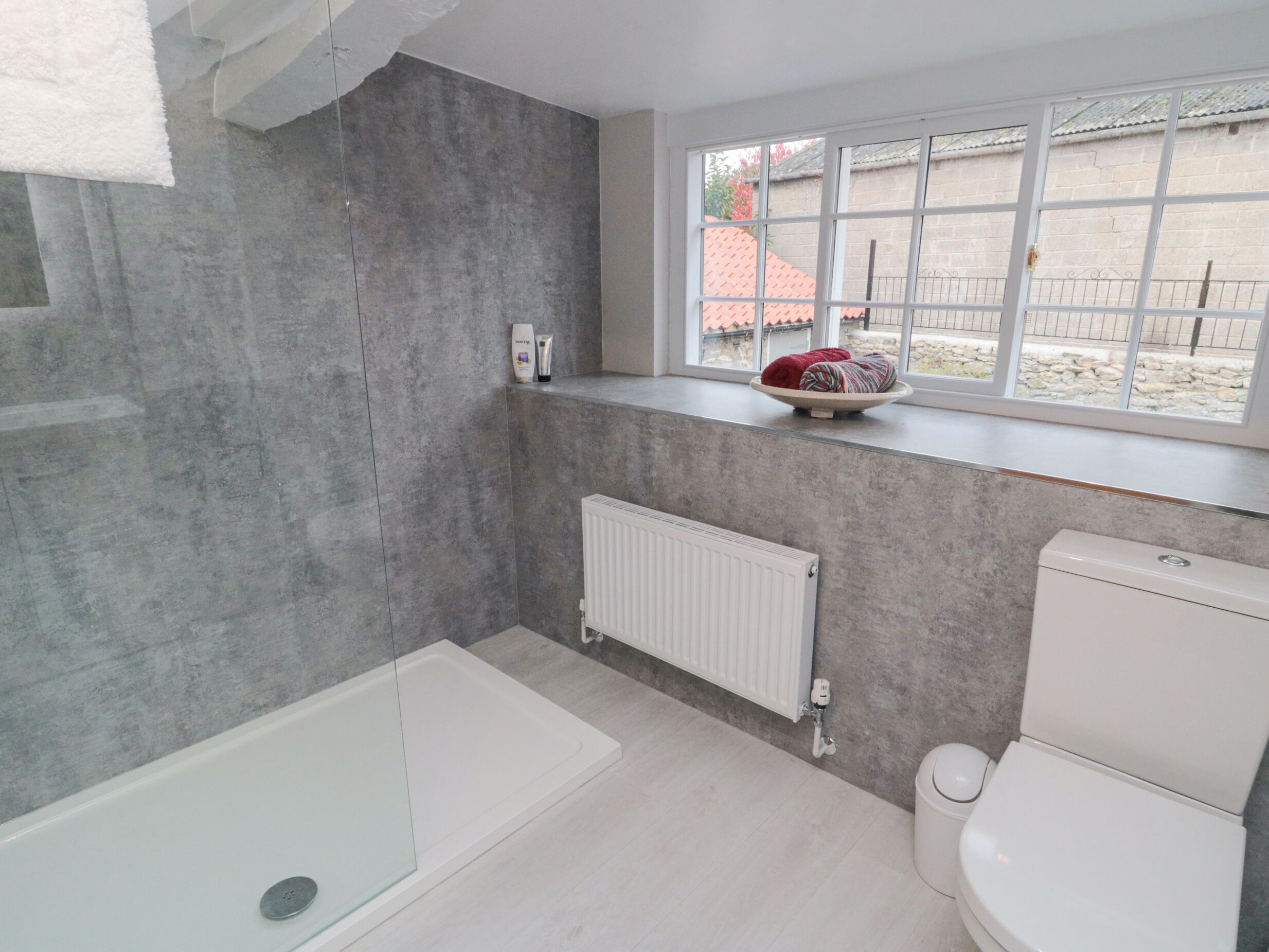 A bathroom with a bathtub, a toilet, a window with a view of the outside, and a radiator.