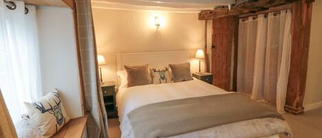 A large bed with a headboard, two bedside tables, and a nightstand. There is a window with curtains on the left side.
