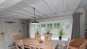 A dining area with a wooden table and chairs, a hanging light fixture, and a view of the outside through large windows. - York House (Pickering)