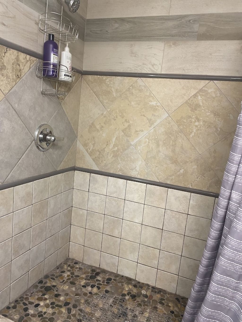 A shower with a pebble-tiled floor, a metal shower head, and a shelf with toiletries.