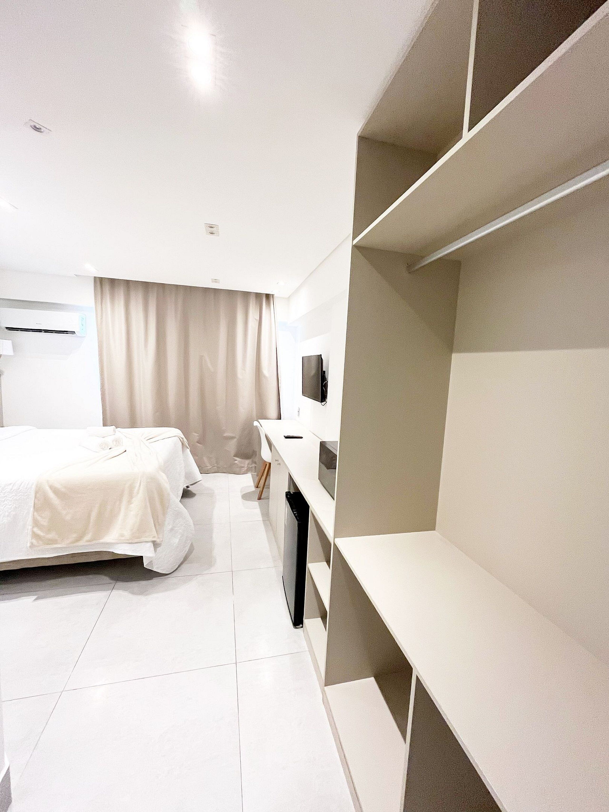 A hotel room with a bed, a desk, a TV, and built-in shelving.