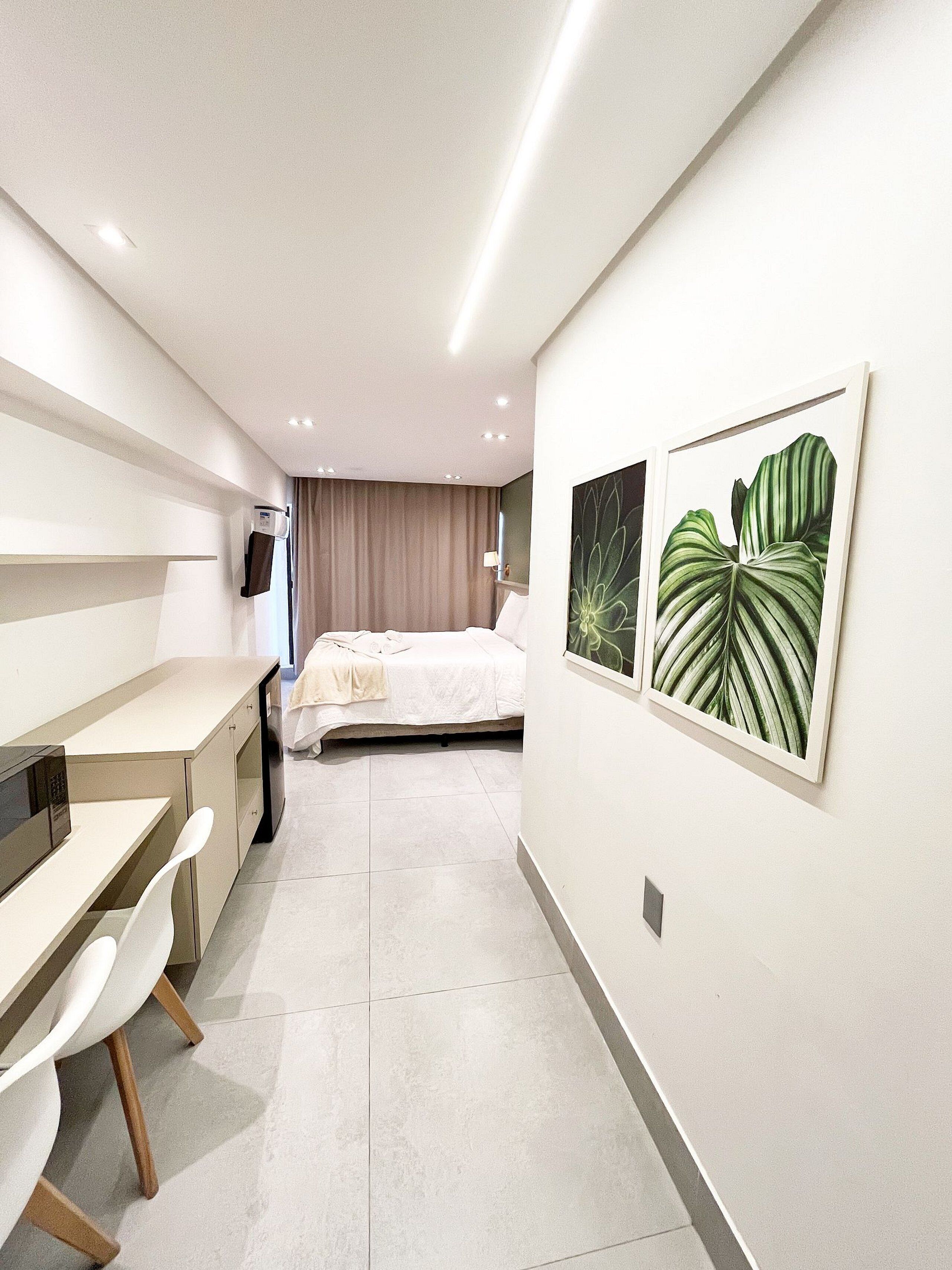A modern hotel room with a bed, a desk, a chair, a microwave, and a wall-mounted TV.