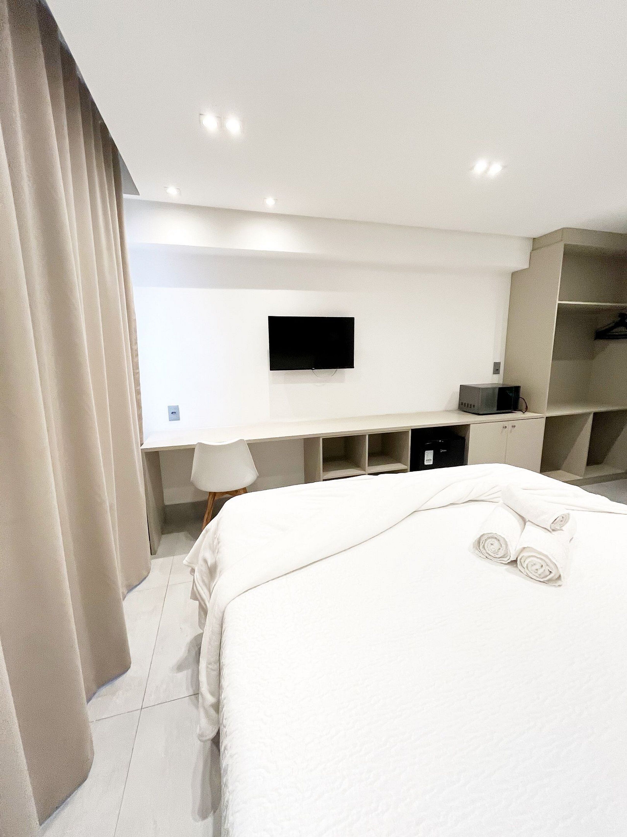 Ett hotellrum med en säng, en platt-TV som är monterad på väggen, ett skrivbord med en stol och en garderob.