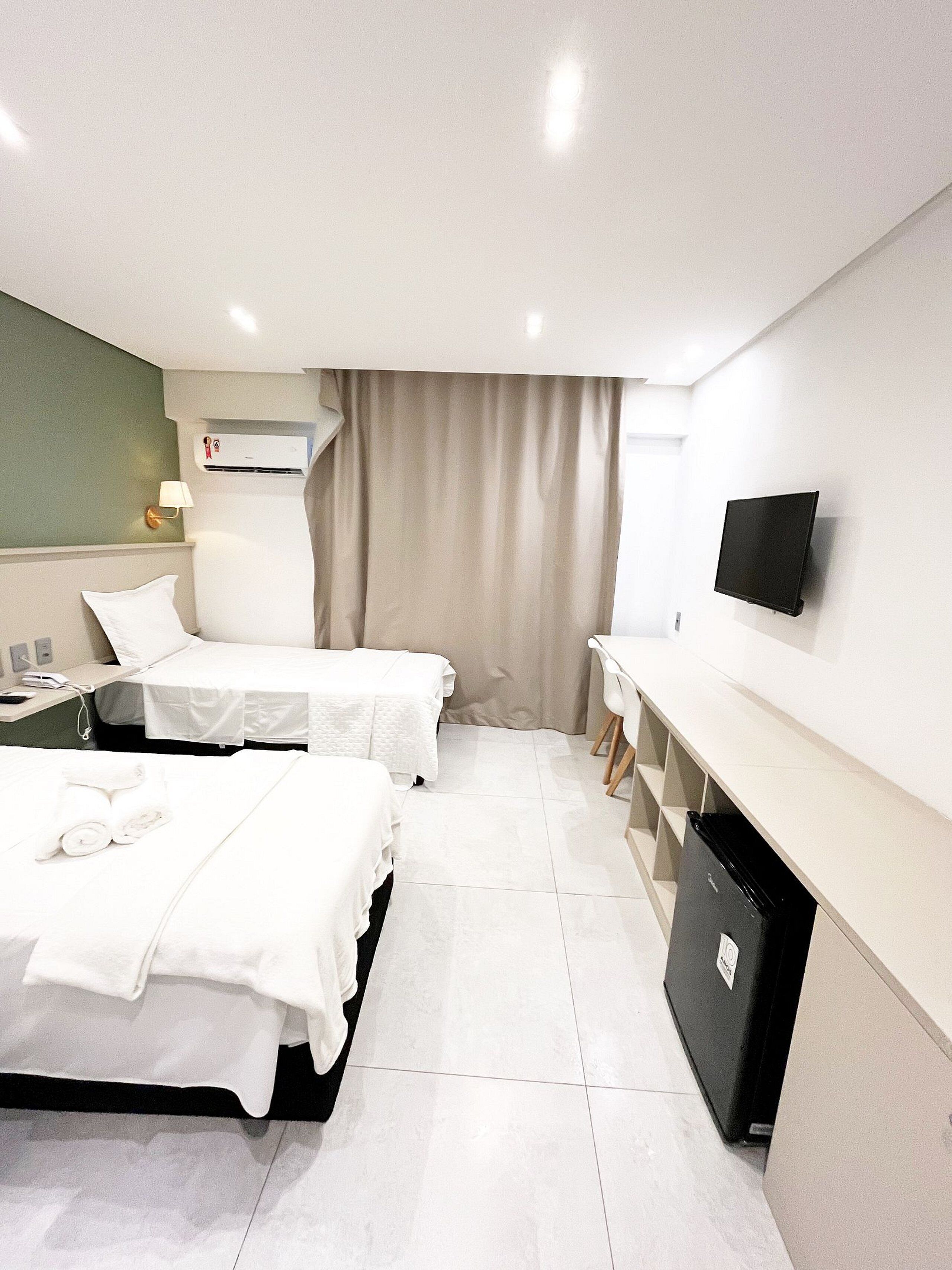A hotel room with two beds, a desk, a TV, and a minibar.