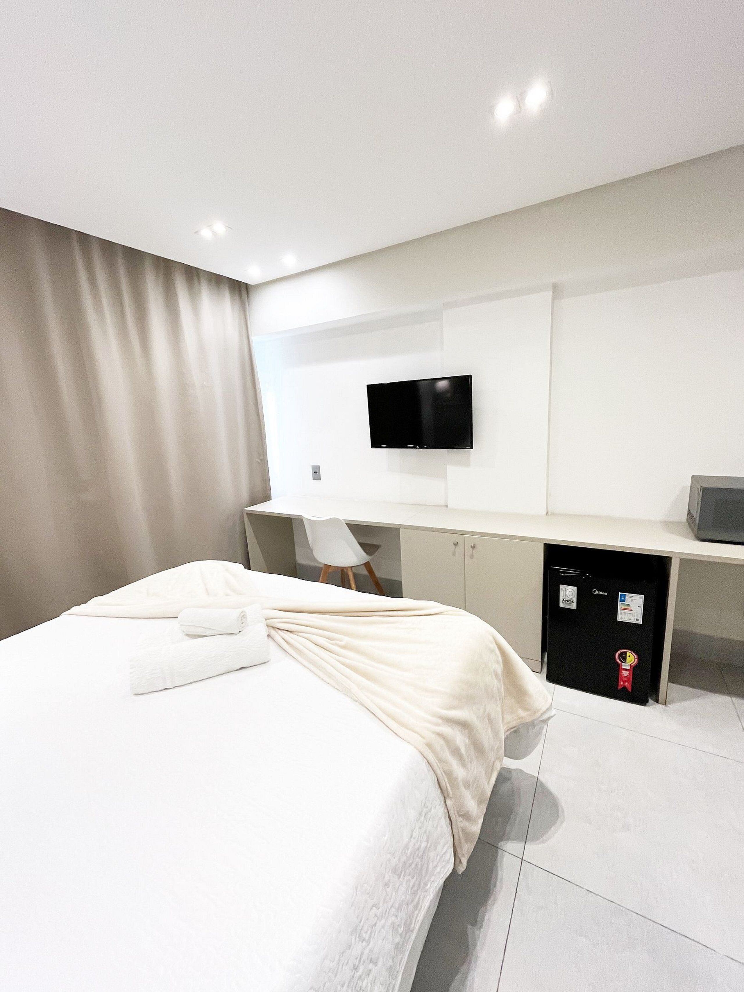 Quarto de hotel moderno com cama, escrivaninha, cadeira, televisão e minibar.