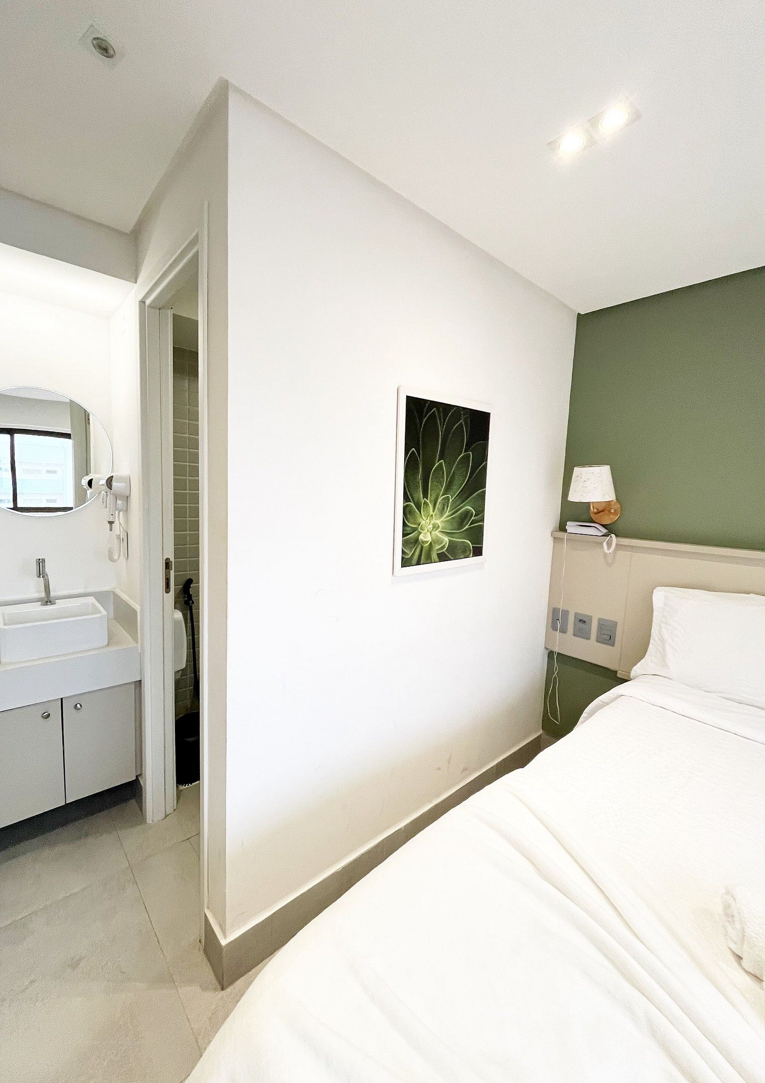 A hotel room with a bed, a bedside table with a lamp, a wall-mounted phone, and a bathroom visible through an open door.