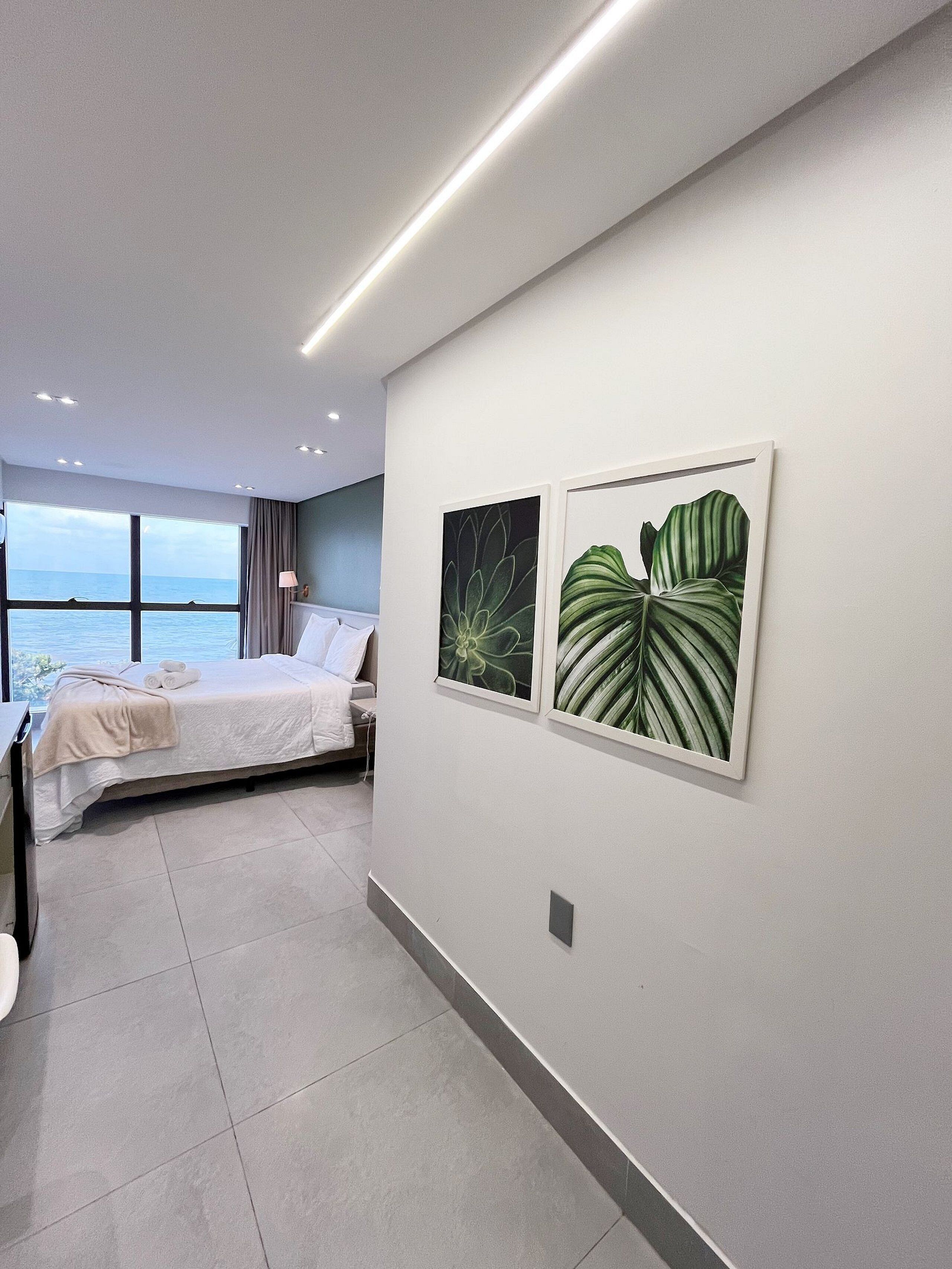Quarto moderno com cama, escrivaninha e vista para o mar.