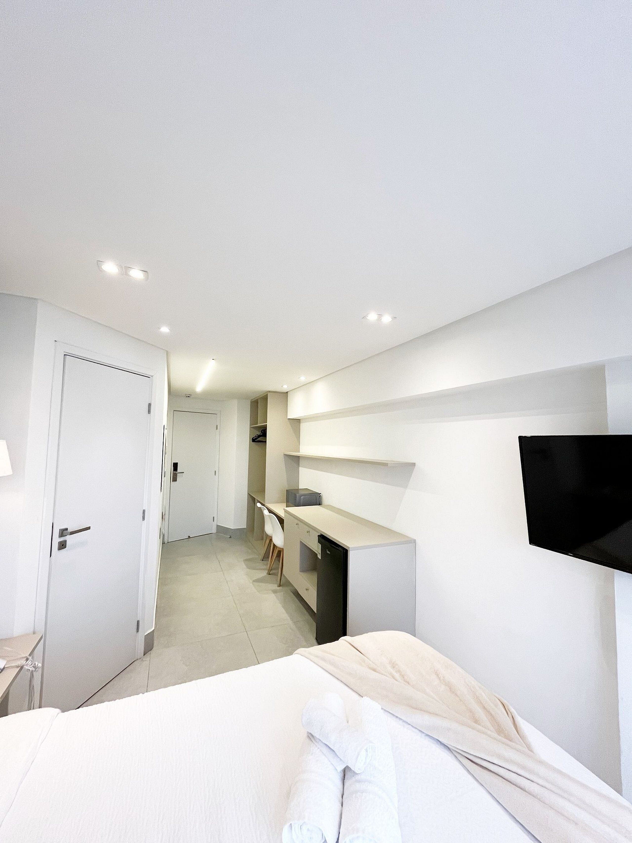 Een moderne hotelkamer met een bed, een bureau, een stoel en een aan de muur bevestigde televisie.