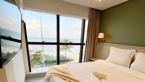 A hotel room with a large bed, a view of the beach, and a window with curtains. - Arpoar Suites By Day By Day (João Pessoa)