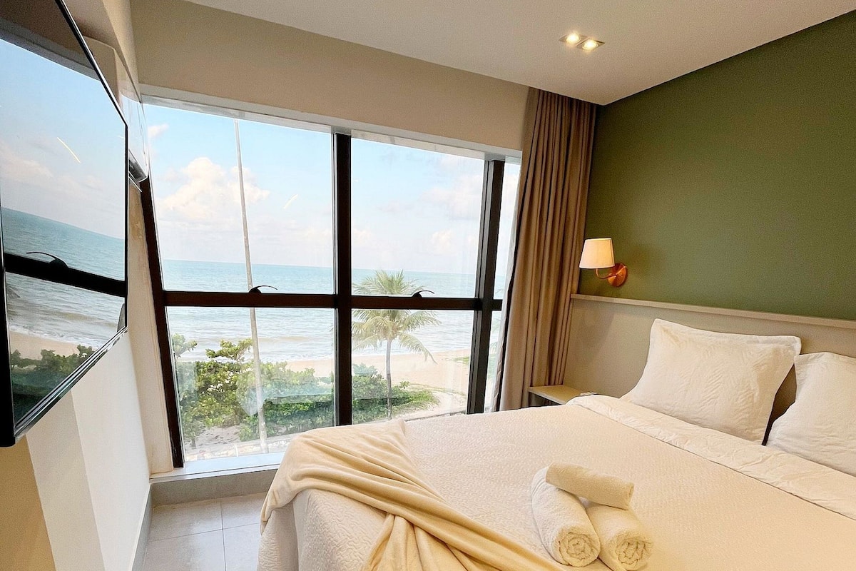 Habitación de hotel con una cama grande, vista a la playa y una ventana con cortinas.