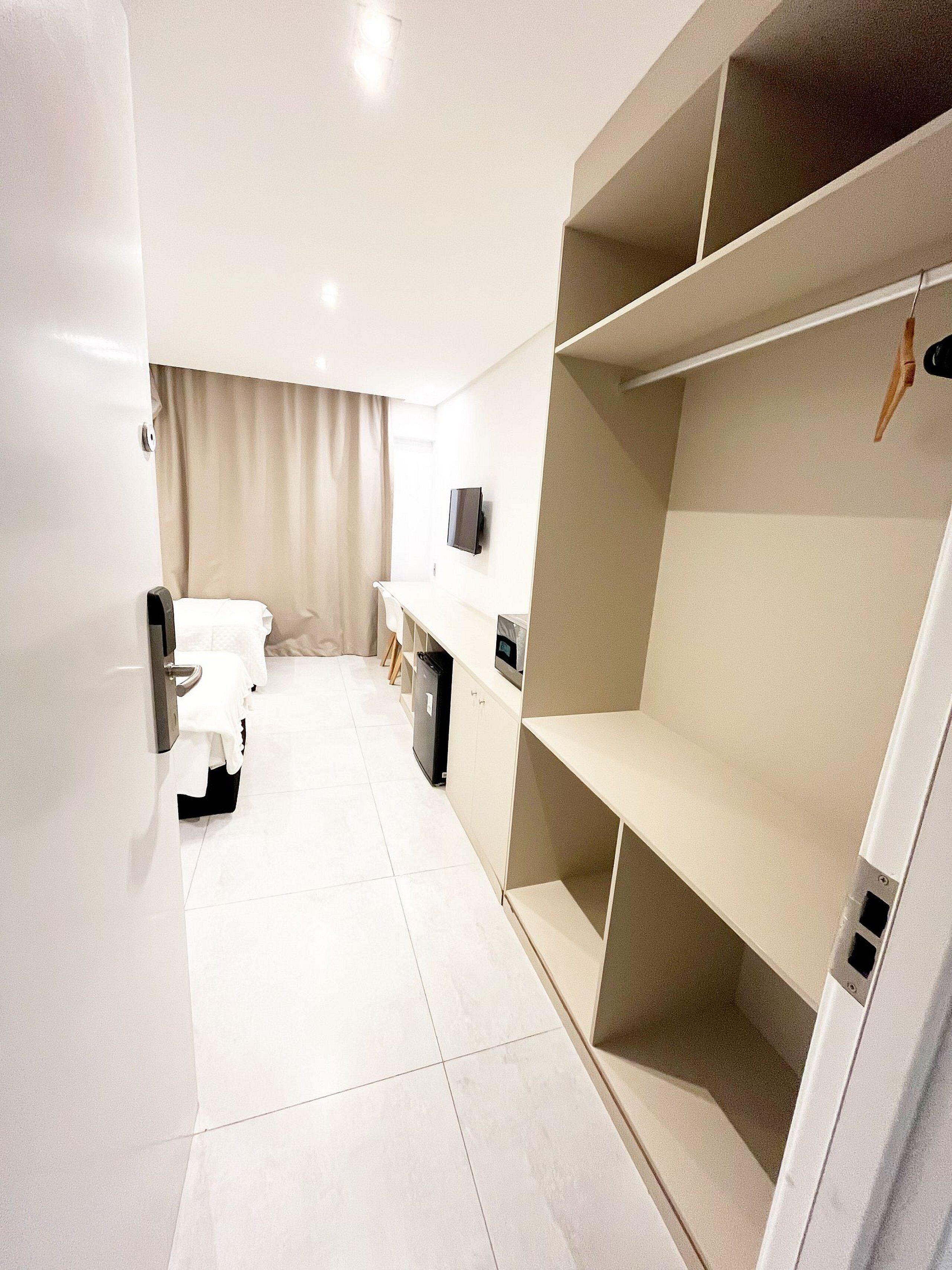 Une chambre d’hôtel moderne équipée d’un lit, d’un bureau, d’une télévision et d’étagères intégrées.