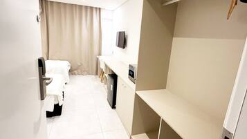Une chambre d’hôtel moderne équipée d’un lit, d’un bureau, d’une télévision et d’étagères intégrées.