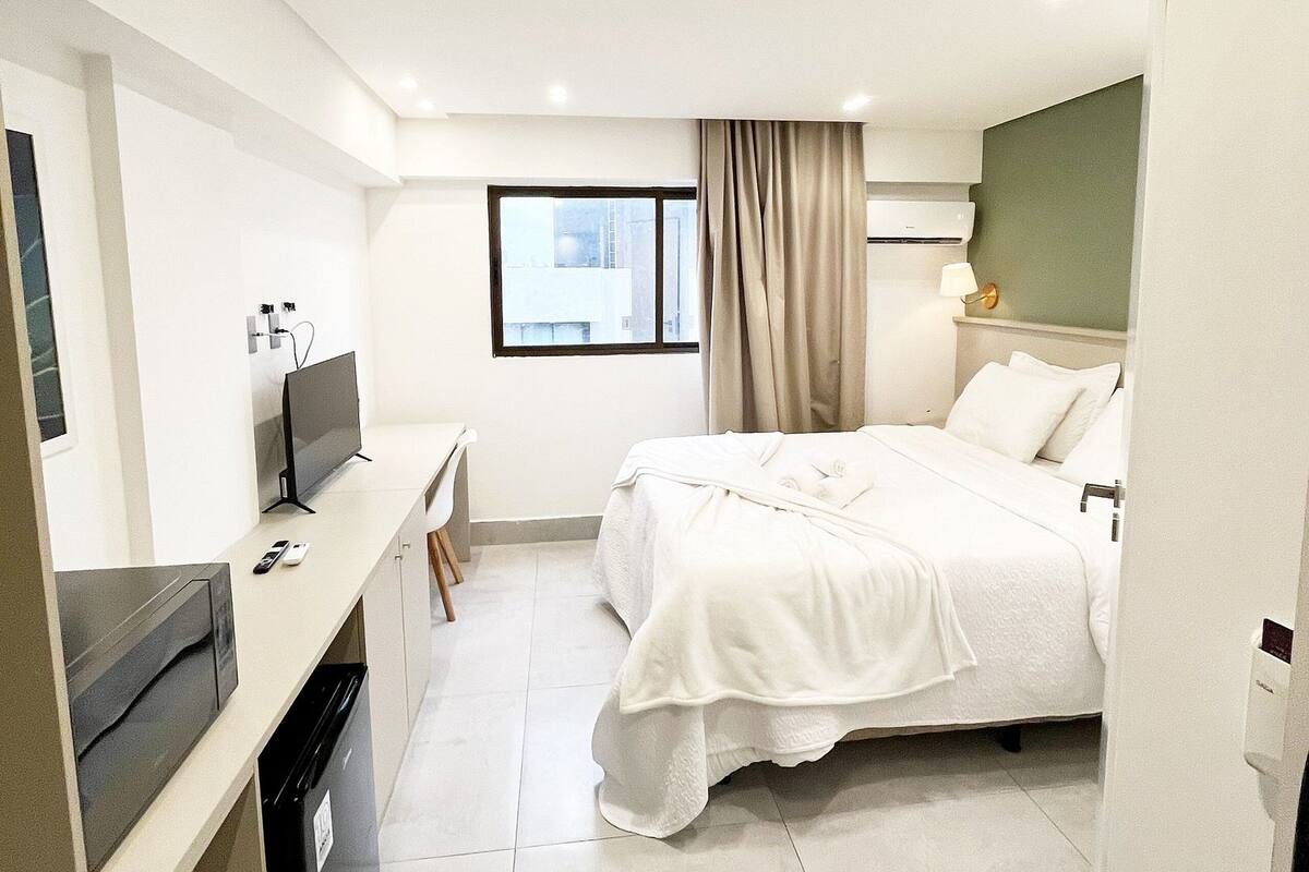 Habitación de hotel con cama, escritorio, televisor y ventana con cortinas.