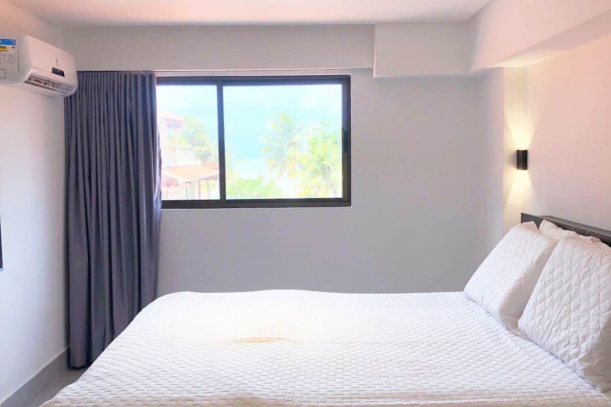 Habitación de hotel con cama, ventana, equipo de aire acondicionado y luz empotrada.