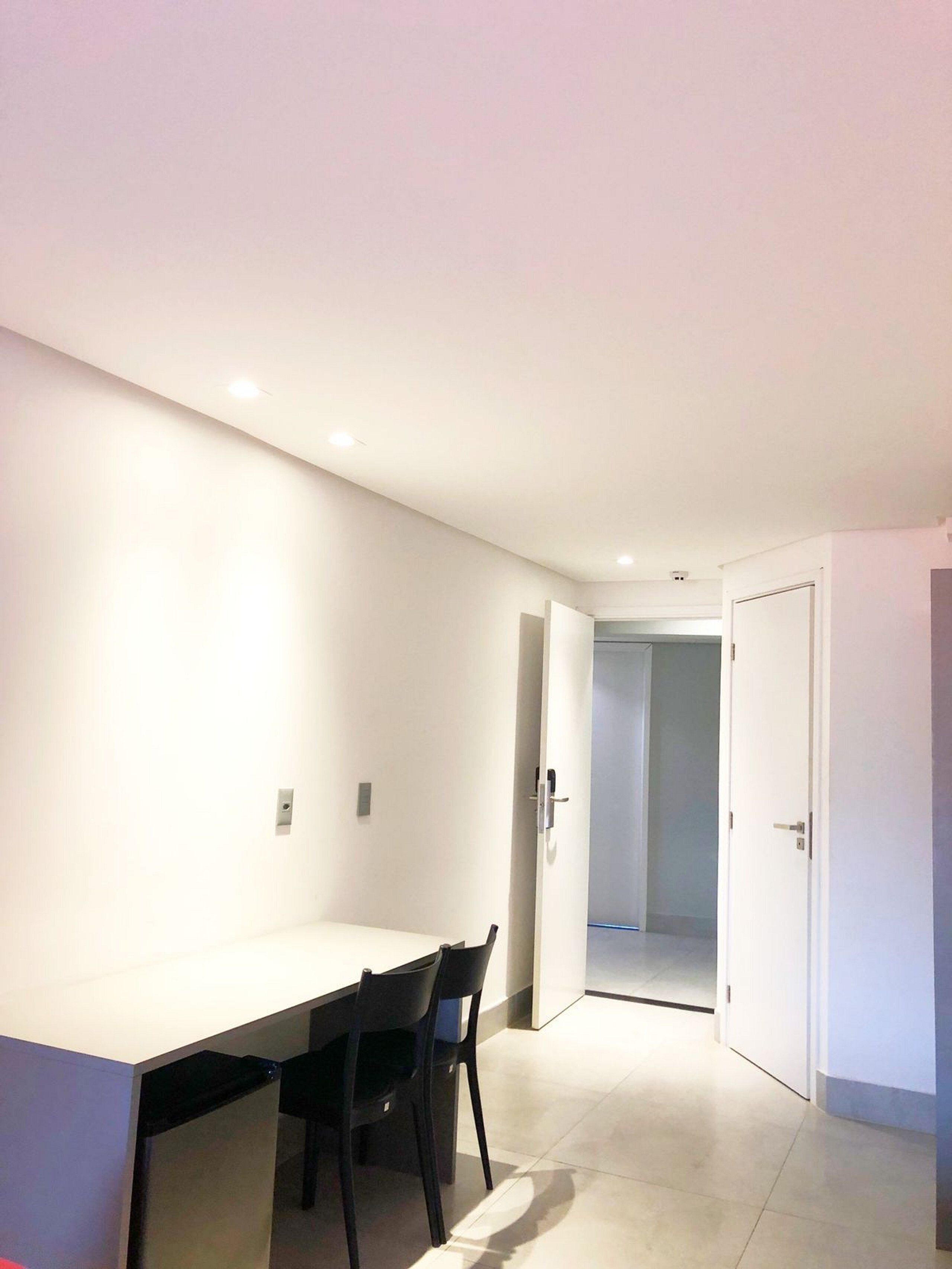 A modern, minimalistic room with a white table and two chairs, a door leading to another room, and a tiled floor.