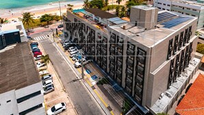 A high-rise building with a rooftop parking area, a beach, and a clear sky. - Arpoar Suites By Day By Day (João Pessoa)