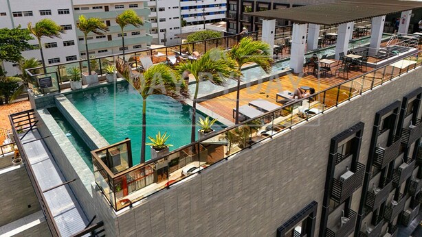 A rooftop pool with lounge chairs and palm trees, surrounded by modern buildings. - Arpoar Suites By Day By Day (João Pessoa)