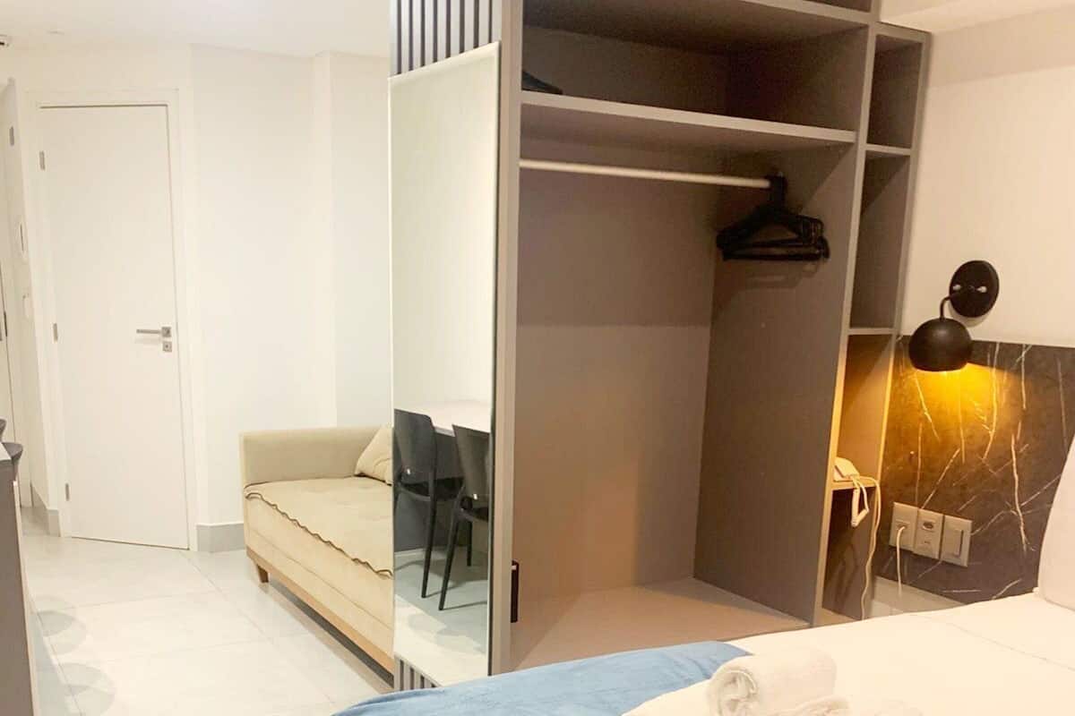 Habitación de hotel con cama, armario, zona de estar y lámpara de pared.