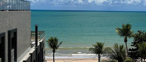 A coastal hotel with a view of the ocean, a beach, and palm trees.