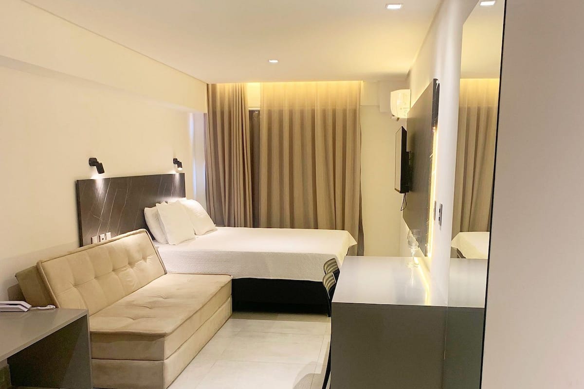 Una habitación de hotel moderna con cama, sofá, televisión y un espejo grande.