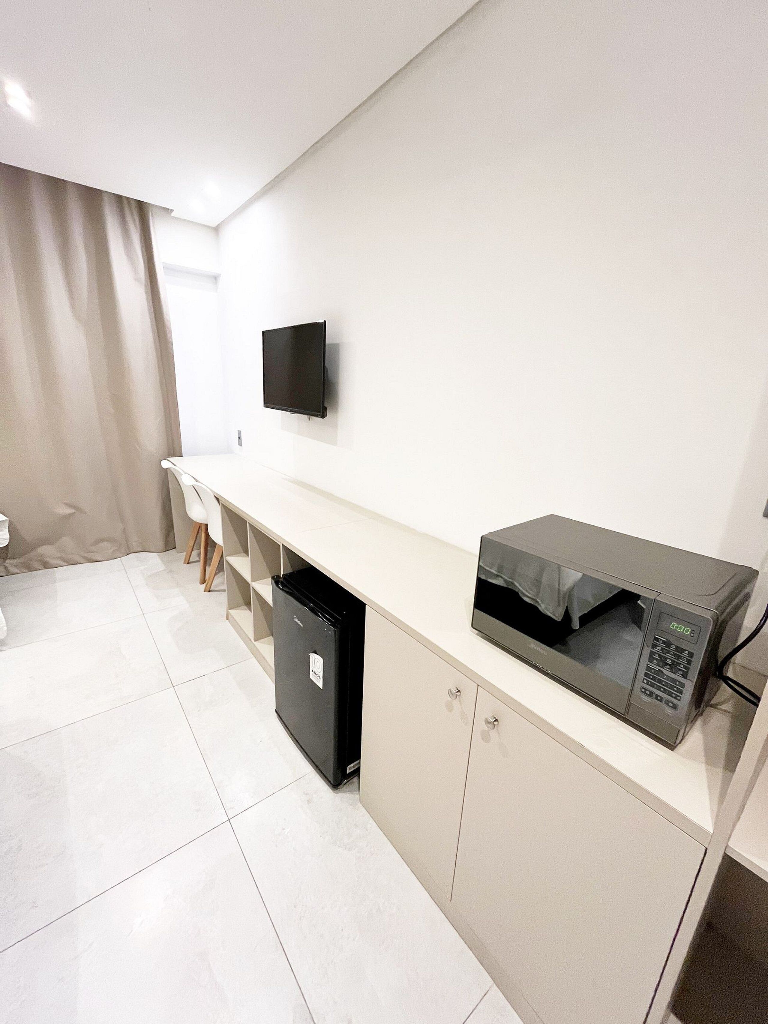 A modern kitchen with a microwave, a small refrigerator, and a flat-screen TV mounted on the wall.