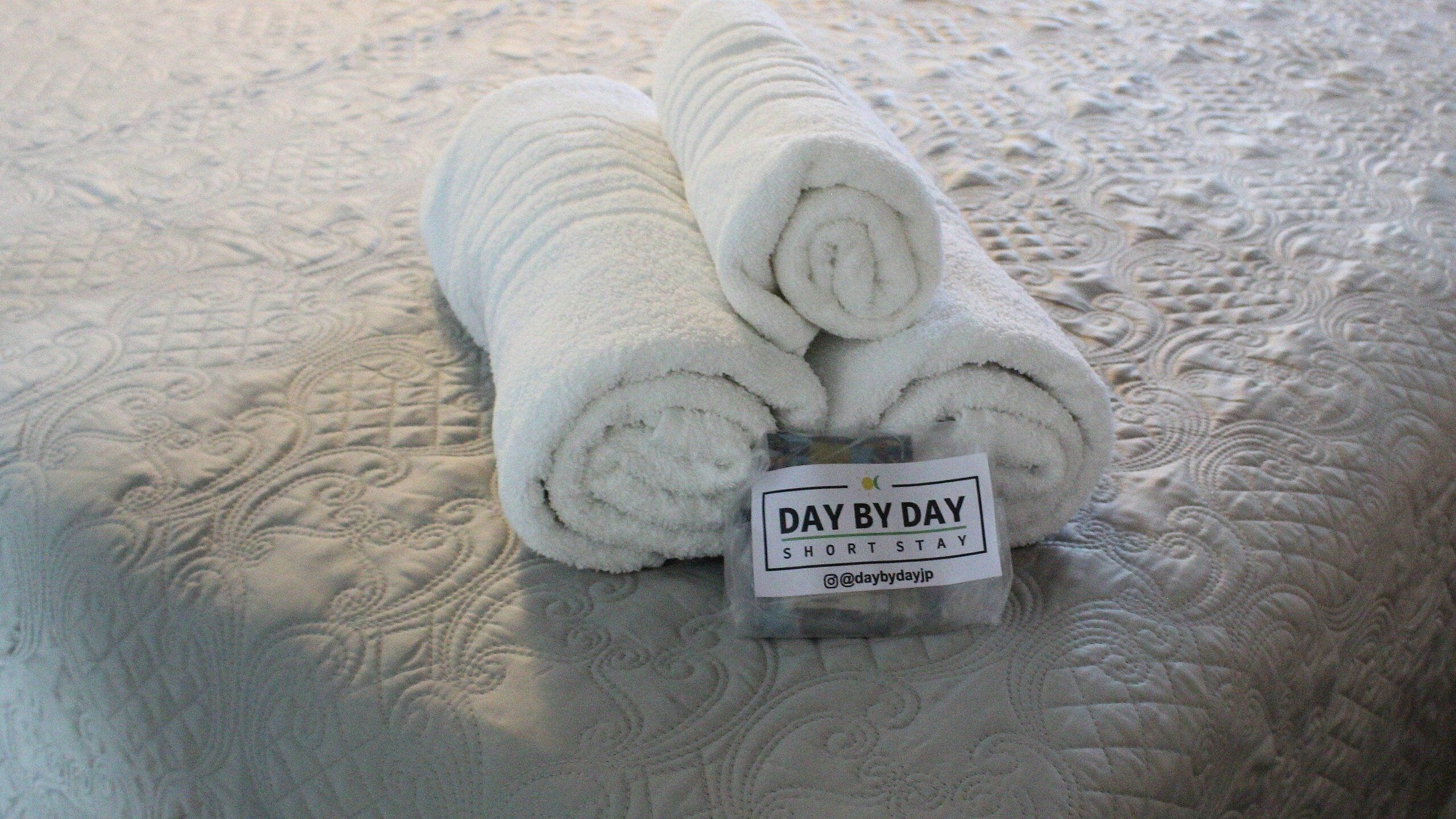 A rolled white towel with a label on a textured bedspread.