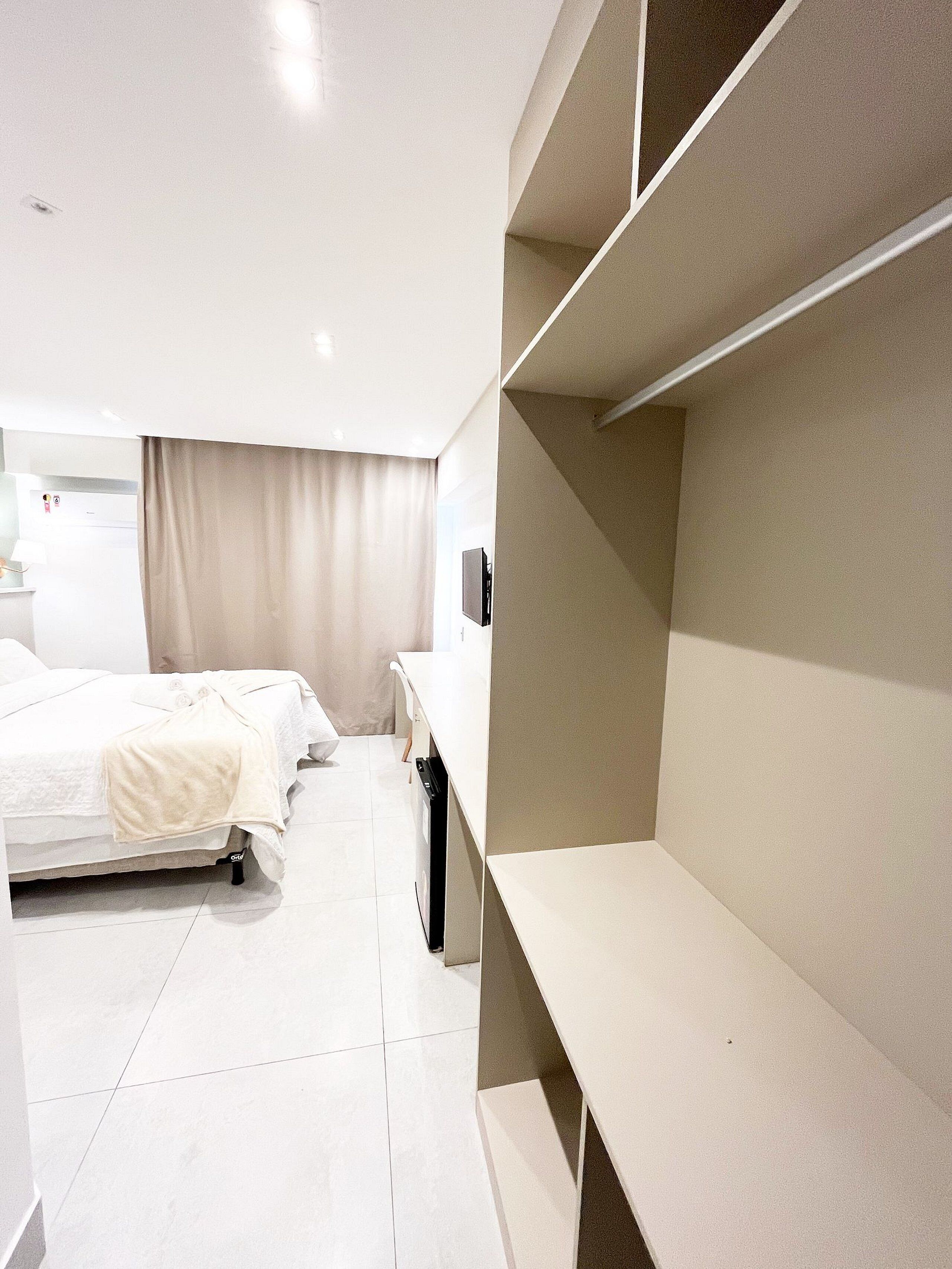 Quarto de hotel moderno com cama, escrivaninha e estantes embutidas.