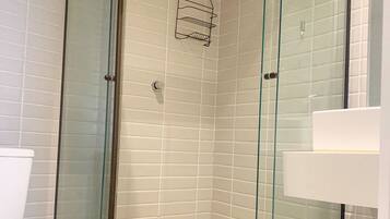 A glass-enclosed shower with white tiled walls and a white toilet visible to the left.