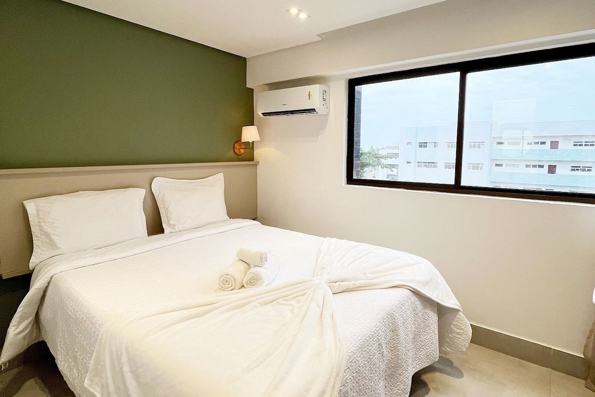 Una habitación de hotel con cama, ventana, aire acondicionado y lámpara.