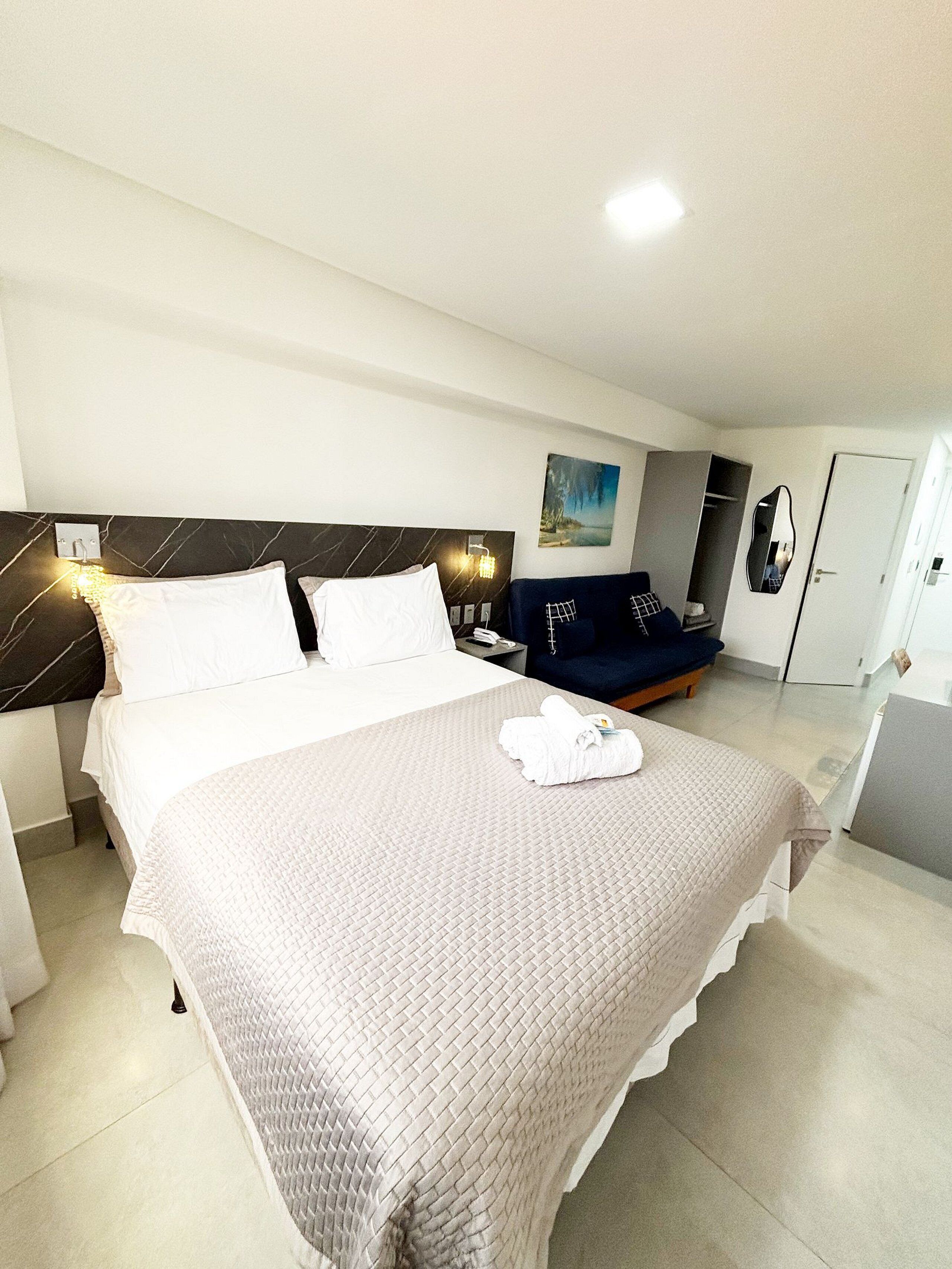 Una habitación de hotel con cama, mesita de noche, lámpara y un cuadro en la pared.