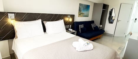 A hotel room with a bed, bedside table, lamp, and a painting on the wall.