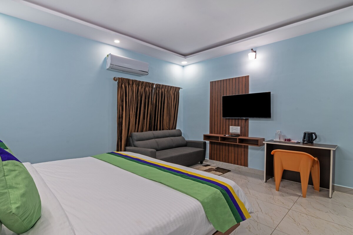 A hotel room with a bed, a desk, a chair, a TV, and an air conditioning unit.