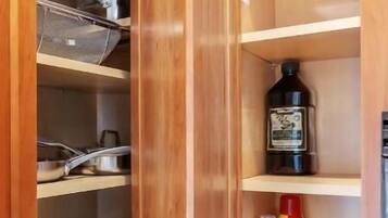 A wooden kitchen cabinet with shelves containing cookware, a bottle of cooking oil, and a can of sauce.