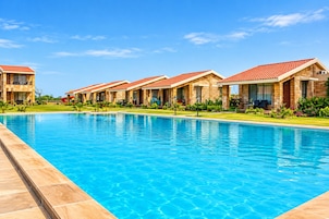 Una piscina con superficie azul cristalina, rodeada por una hilera de edificios de piedra con tejados de tejas rojas.