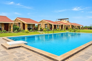 A swimming pool with a stone border, a lounge chair, and a row of buildings with red-tiled roofs.