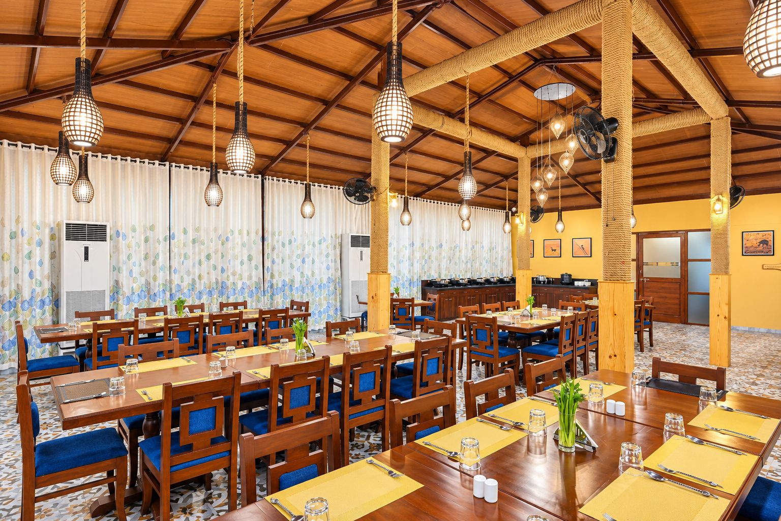 A spacious dining area with multiple tables and chairs, wooden beams on the ceiling, and hanging pendant lights.